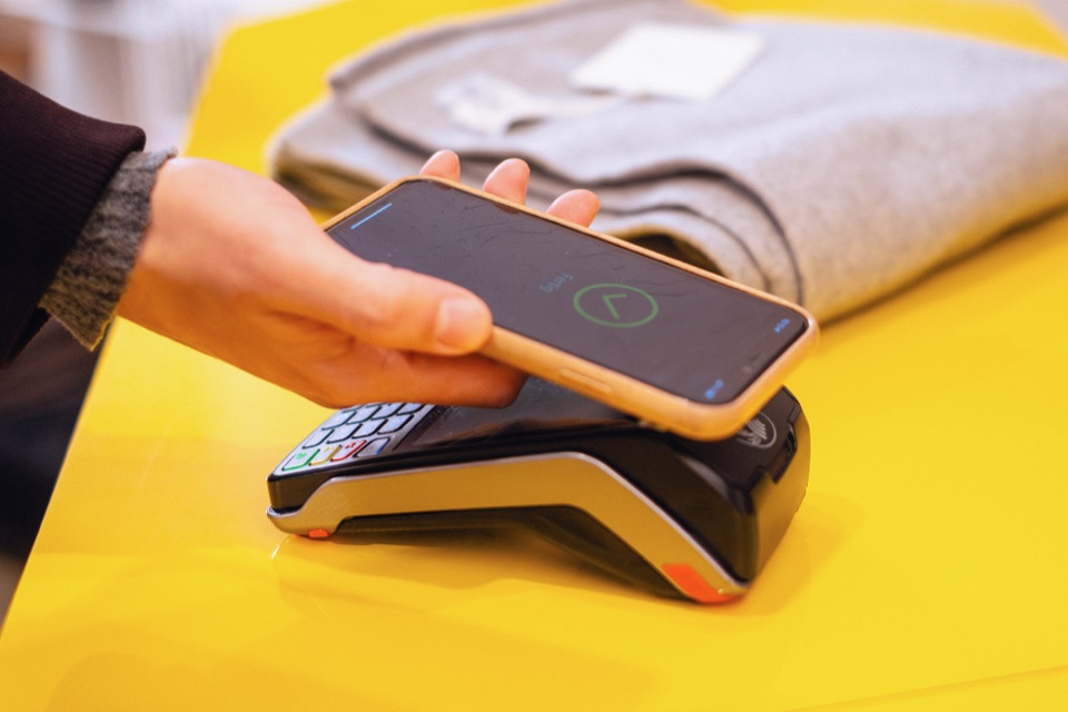 Hand hält ein Smartphone an ein Kartenlesegerät, auf dem Display erscheint die Bestätigung der Zahlung