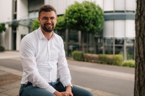 Portr&auml;t eines l&auml;chelnden Mannes mit Brille vor einem B&uuml;rogeb&auml;ude