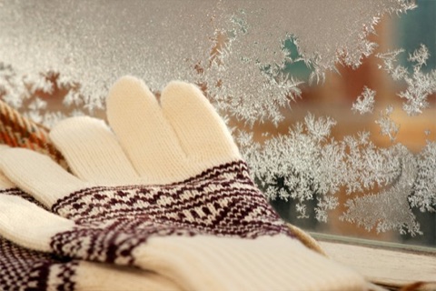 Wollhandschuhe vor einem Fenster mit winterlichen Eisblumen