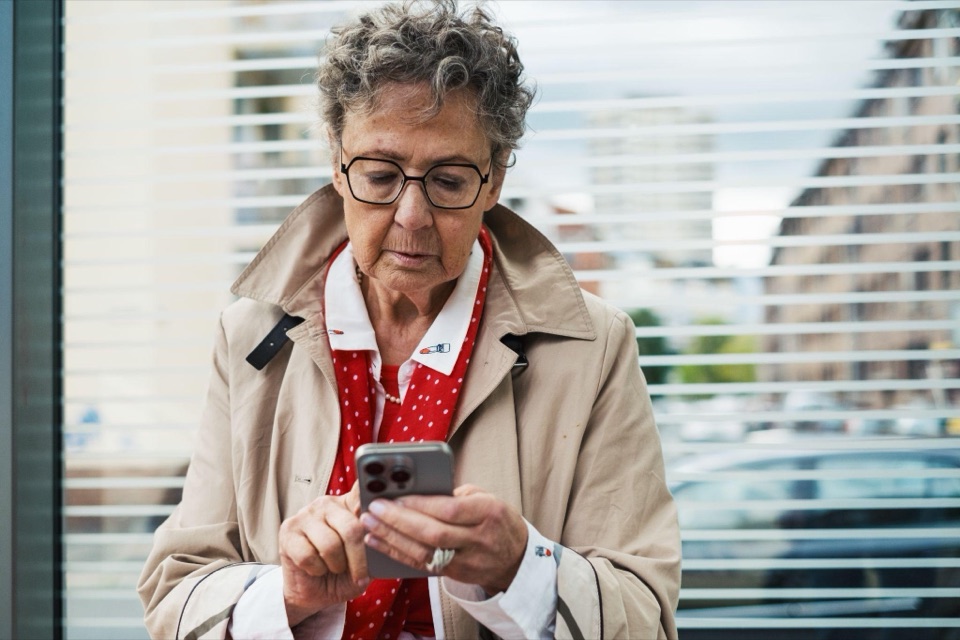 &Auml;ltere Frau pr&uuml;ft aufmerksam eine Nachricht auf dem Smartphone