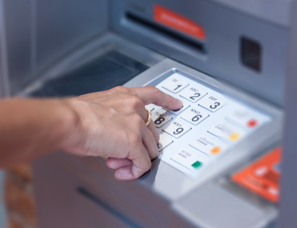 Hand tippt eine PIN auf dem Tastenfeld eines Geldautomaten ein