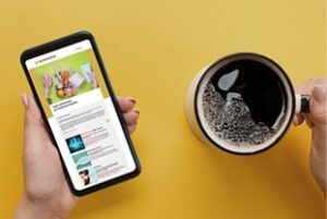 Smartphone mit ge&ouml;ffnetem Newsletter neben einer Tasse Kaffee